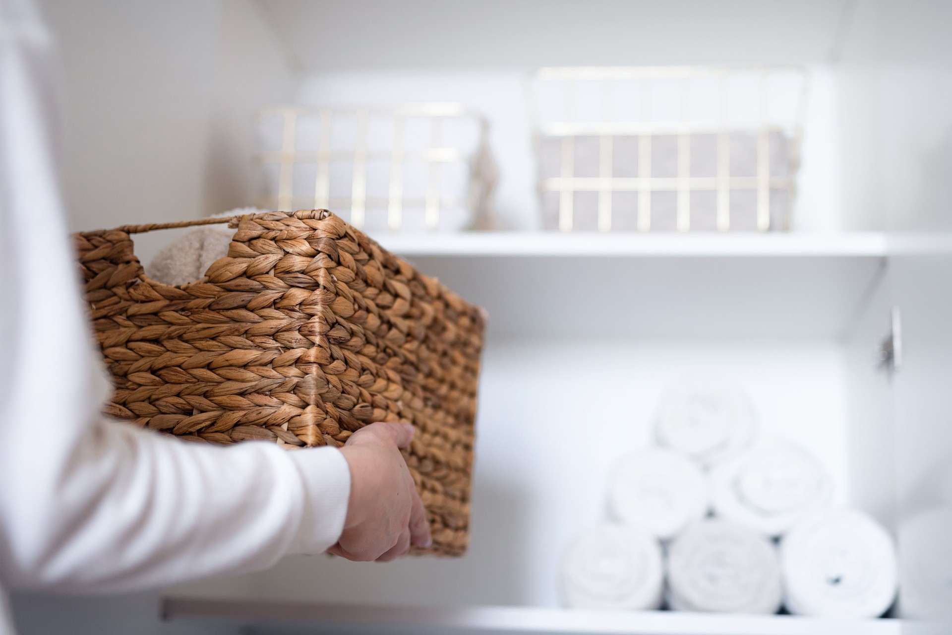 Woman organizing clothes on shelves in white opened wardrobe, folding laundry in baskets. Space organization and storage system.