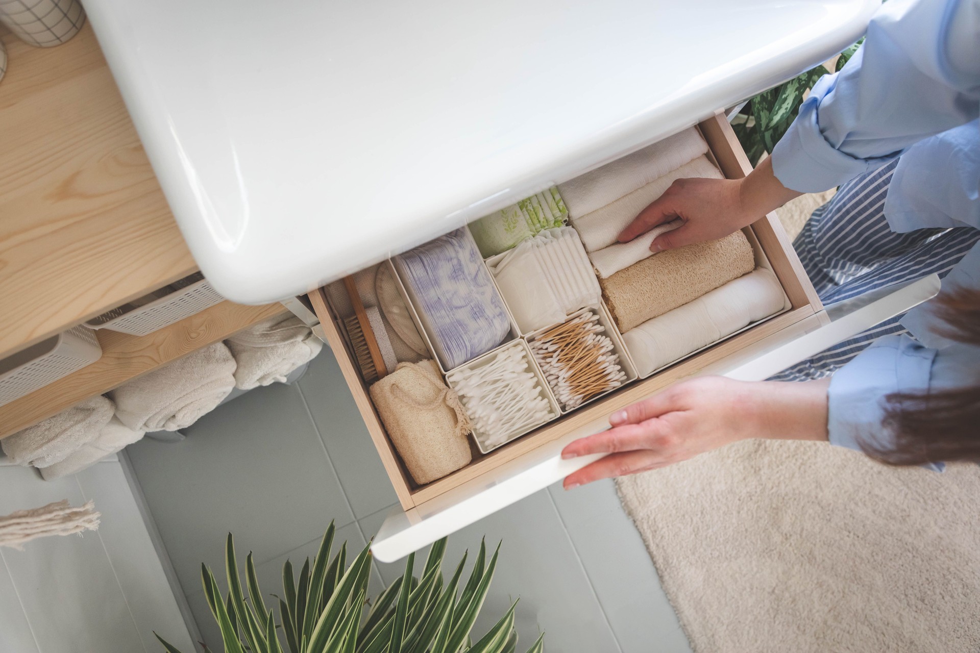 Top view of woman hands neatly organizing bathroom amenities and toiletries in drawer in bathroom.