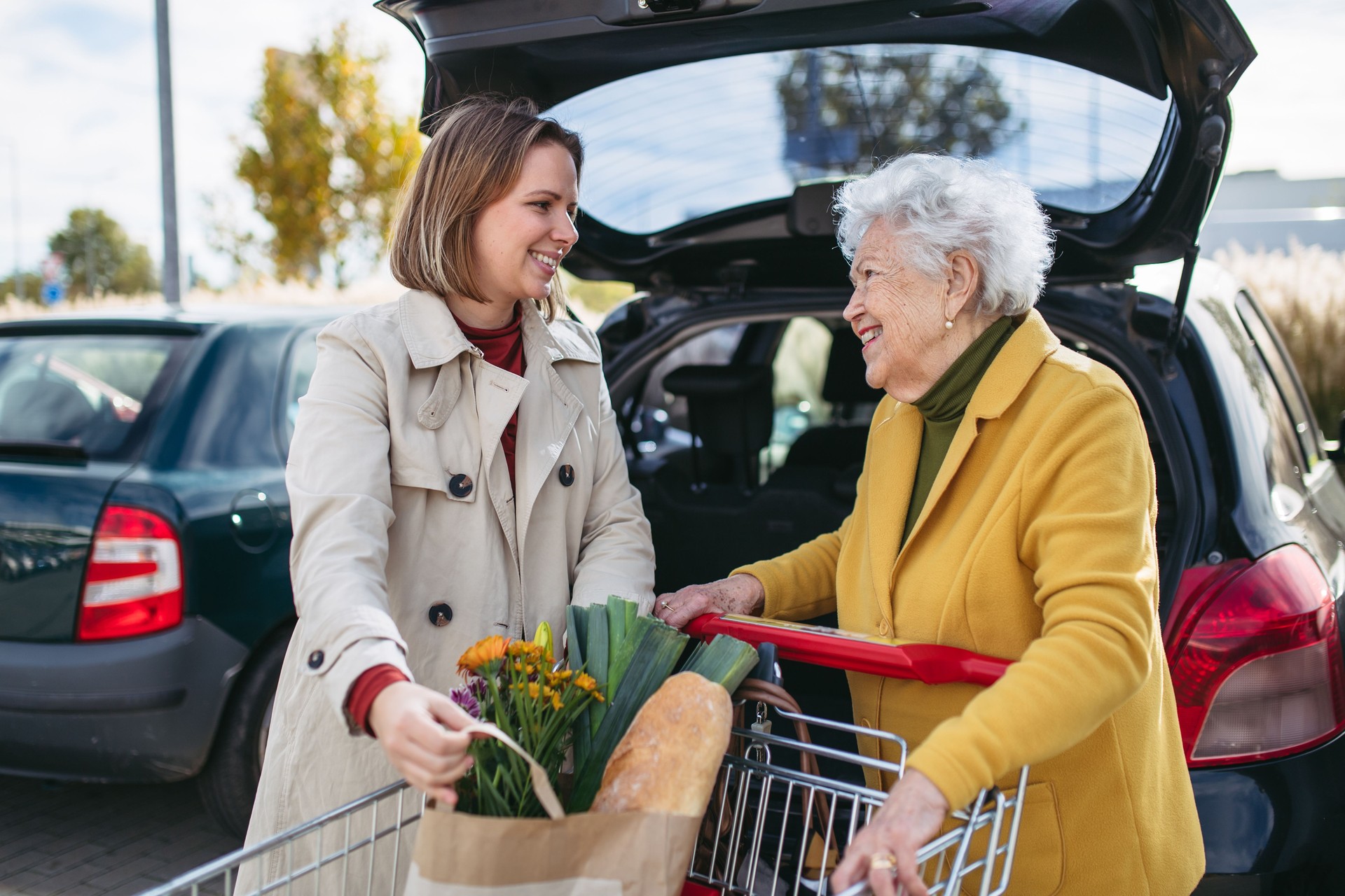Mature granddaughter helping grandmother load groceries in to the car. Senior woman shopping at the shopping center.